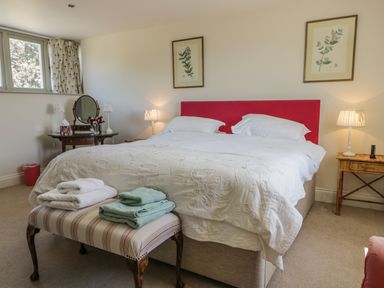 A bedroom with a double bed with red headboard two bedside tables with lamps a dressing table and a bench with folded towels at Cow Byre in Malton