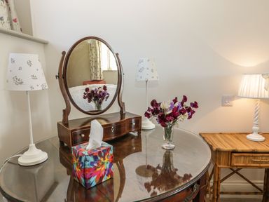 A dressing table with an oval mirror flowers in a vase two lamps and a colorful tissue box at Cow Byre in Malton
