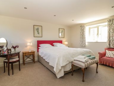 A bedroom with a double bed a striped bench with towels a wooden dressing table and a red armchair at Cow Byre in Malton