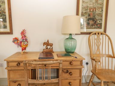 A wooden desk with a wooden chair a lamp a colorful rooster decoration a horse statue and framed pictures on the wall at Cow Byre in Malton
