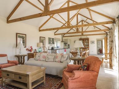An open living room and kitchen with sofa armchairs wooden tables beams and dining area at Cow Byre in Malton