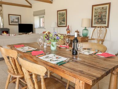 A wooden dining table set with plates wine glasses and cutlery in a living room with a sofa television and fireplace at Cow Byre in Malton
