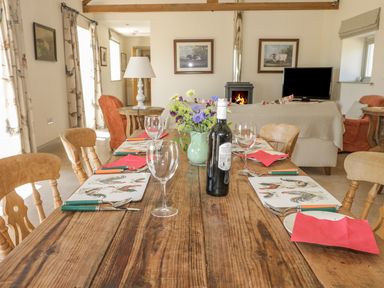 A dining table with place settings and a bottle of wine in a living room with a fireplace at Cow Byre in Malton