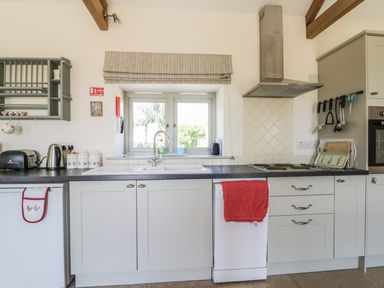 A kitchen with a sink under a window a stove a dishwasher and various utensils at Cow Byre in Malton