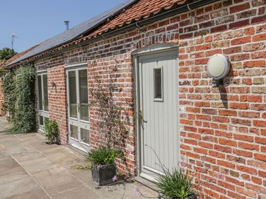 An exterior view of a brick building with white door and windows and plants outside at Cow Byre in Malton