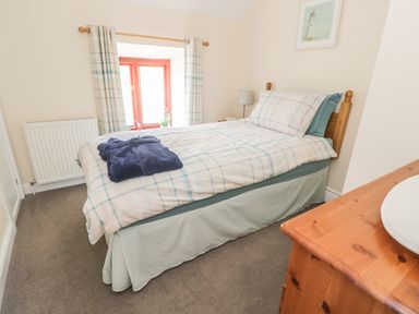 A bedroom with a single bed a blue bathrobe on the bed a window with curtains and a wooden dresser at Oak Cottage in Bryngwenith near Newcastle Emlyn