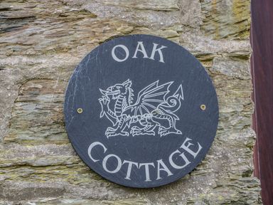 A round black sign with a dragon and the words Oak Cottage on a stone wall at Oak Cottage in Bryngwenith near Newcastle Emlyn