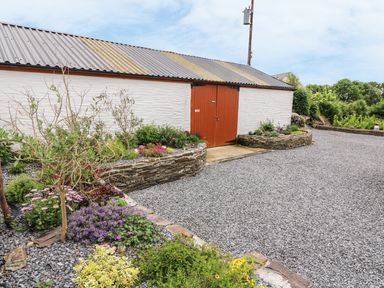 A gravel driveway with flower beds and a white building with a brown door at Oak Cottage in Bryngwenith near Newcastle Emlyn
