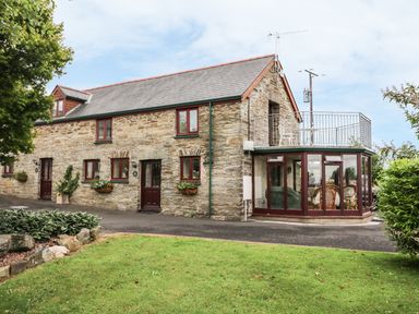 A stone cottage with glass conservatory and balcony overlooking a lawn at Oak Cottage in Bryngwenith near Newcastle Emlyn