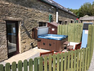 An outdoor area with a stone wall building a hot tub fenced seating area and a door at Oak Cottage Bryngwenith near Newcastle Emlyn