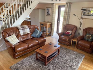 A living room with brown leather sofa and chairs a wooden coffee table and staircase at Oak Cottage in Bryngwenith near Newcastle Emlyn