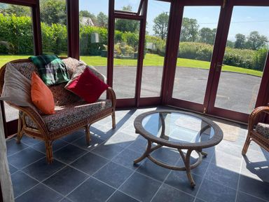 A sunroom with wicker chairs with cushions and a round glass coffee table with a view of a garden at Oak Cottage Bryngwenith near Newcastle Emlyn