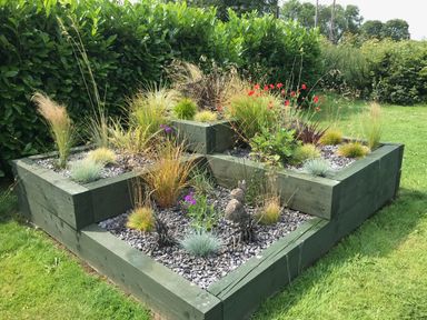 A raised garden bed with assorted plants and a small statue in a grassy yard at Oak Cottage Bryngwenith near Newcastle Emlyn