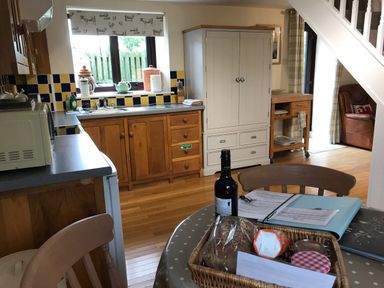 A kitchen with wooden cabinets a white cupboard and a dining table with a basket of food items at Oak Cottage in Bryngwenith near Newcastle Emlyn