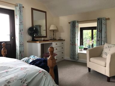 A bedroom with a bed armchair dresser mirror and window at Oak Cottage in Bryngwenith near Newcastle Emlyn