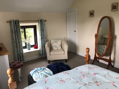 A bedroom with a bed with floral bedding an armchair and a full-length wooden mirror at Oak Cottage in Bryngwenith near Newcastle Emlyn