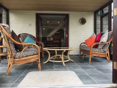 A sunroom with wicker furniture and cushions and a glass top table at Oak Cottage in Bryngwenith near Newcastle Emlyn