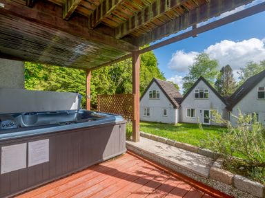 An outdoor covered wooden deck with a hot tub overlooking houses and green lawn at Brookside in Honicombe Manor near Gunnislake