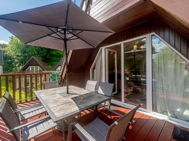An outdoor patio with a table and chairs under an umbrella with glass doors leading inside at Brookside in Honicombe Manor near Gunnislake