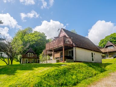A group of houses with balconies on a grassy hill under a blue sky at Brookside in Honicombe Manor near Gunnislake