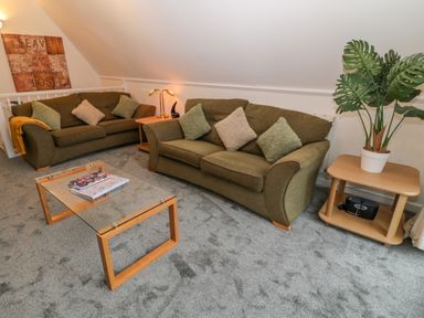 A living room with two sofas a glass coffee table side tables a large plant and a wall decoration at Brookside in Honicombe Manor near Gunnislake