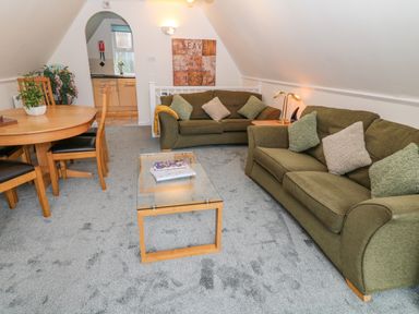 A living room with two green sofas a glass coffee table and a wooden dining table with chairs at Brookside in Honicombe Manor near Gunnislake