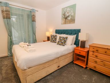 A bedroom with a double bed two bedside tables with lamps a chest of drawers and curtains at Brookside in Honicombe Manor near Gunnislake