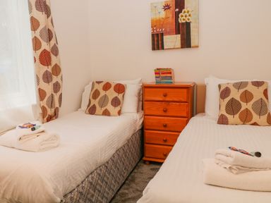 A bedroom with two single beds a wooden chest of drawers and patterned curtains at Brookside in Honicombe Manor near Gunnislake