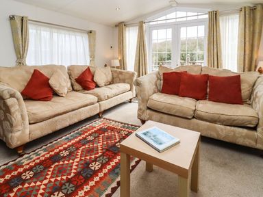 A living room with two beige sofas with red and beige cushions and a wooden table with a book in Broad Down Berrow