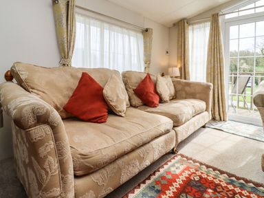 A beige patterned sofa with red and beige cushions in a living room with curtains and glass doors showing a garden at Broad Down in Berrow