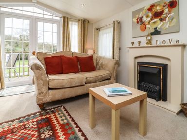 A living room with a sofa red cushions coffee table fireplace and glass doors at Broad Down in Berrow