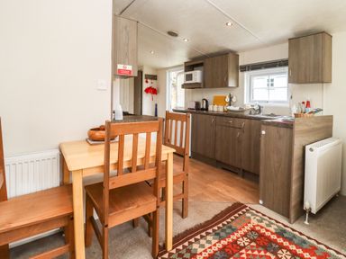 A kitchen with wooden cabinets a dining table with chairs and a patterned rug at Broad Down in Berrow