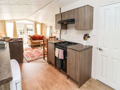 A kitchen with wooden cabinets and a stove leading to a living area with a sofa and a rug at Broad Down in Berrow
