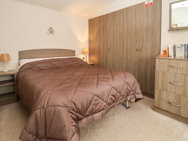 A bedroom with a double bed and brown bedding two bedside tables with lamps a large wardrobe and a chest of drawers with books at Broad Down Berrow