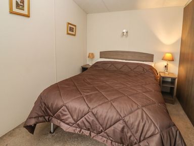 A bedroom with a double bed brown quilt two bedside tables and lamps at Broad Down in Berrow