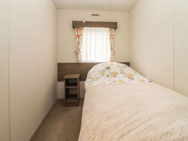 A small bedroom with a single bed a bedside table and a window with floral curtains at Broad Down in Berrow