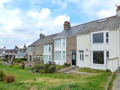 A row of connected houses with front gardens and grass in front at Sandy Bank in Rhosneigr
