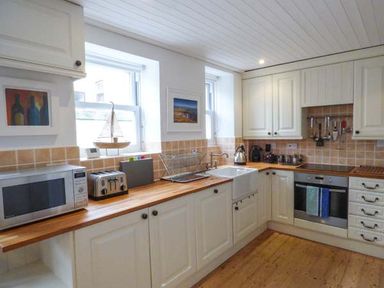A kitchen with white cabinets wooden countertops a microwave toaster sink oven and utensils hanging on the wall at Sandy Bank in Rhosneigr