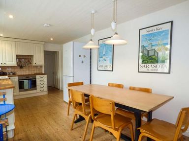 A kitchen with wooden dining table and chairs white cabinets and refrigerator at Sandy Bank in Rhosneigr