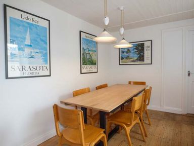 A dining room with a wooden table six chairs three framed pictures on the wall and two pendant lights at Sandy Bank in Rhosneigr