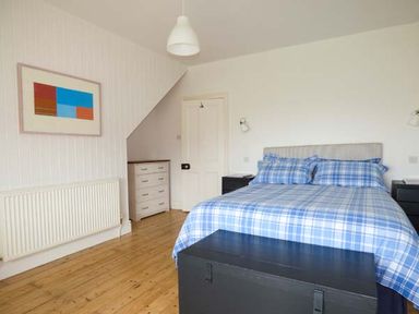 A bedroom with a double bed and plaid bedding two nightstands a chest of drawers and a framed artwork on the wall at Sandy Bank in Rhosneigr