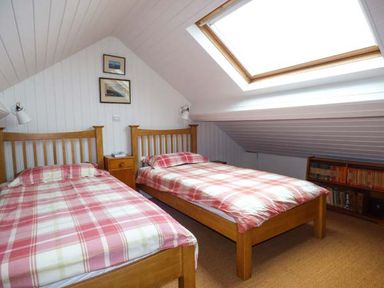 A bedroom with two wooden beds with red plaid bedding a skylight and a bookshelf at Sandy Bank in Rhosneigr