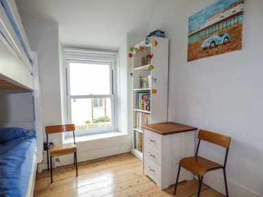 A small bedroom with bunk beds a window two chairs a white bookshelf and a white drawer cabinet at Sandy Bank in Rhosneigr