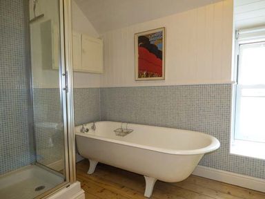 A bathroom with a clawfoot bathtub shower enclosure and a framed picture on the wall at Sandy Bank in Rhosneigr