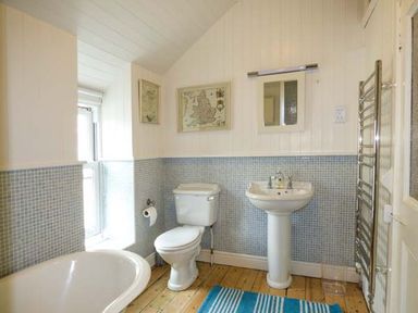 A bathroom with a bathtub toilet sink mirror towel rack and framed maps on the wall at Sandy Bank in Rhosneigr