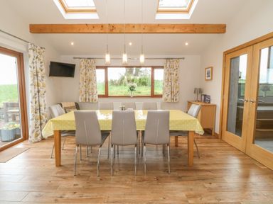 A dining room with a table covered by a yellow tablecloth and eight chairs at Caer Moel in Caernarfon