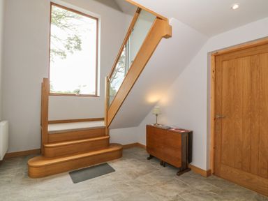 A staircase with wooden steps and glass railing next to a wooden door and a small table with a lamp in a hallway at Caer Moel in Caernarfon