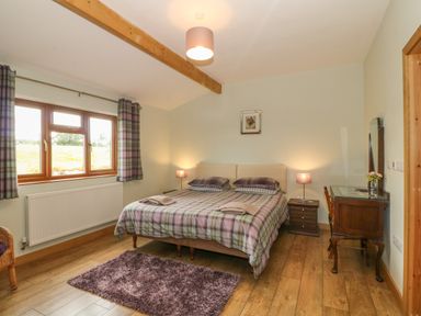 A bedroom with a double bed bedside tables lamps a wooden dresser and a window with plaid curtains at Caer Moel in Caernarfon