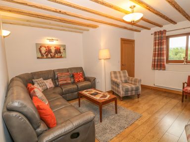 A living room with a leather sectional sofa with cushions a plaid armchair a wooden coffee table and a window with checked curtains at Caer Moel in Caernarfon