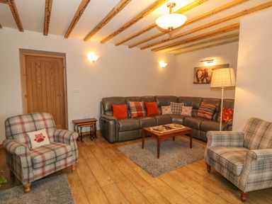 A living room with wooden floor beams plaid armchairs a gray sectional sofa and a wooden coffee table at Caer Moel in Caernarfon